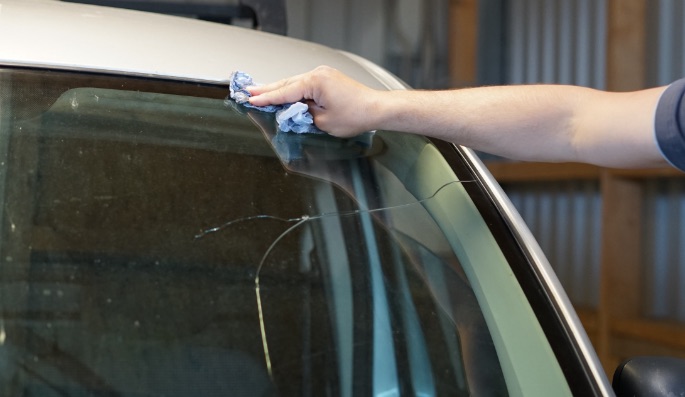 Hand prüft Riss in einer Windschutzscheibe in der Werkstatt